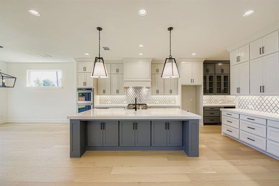 Kitchen featuring gray cabinetry, recessed lighting, hanging light fixtures, a kitchen island with sink, and light wood finished floors Kitchen featuring gray cabinetry, recessed lighting, hanging light fixtures, a kitchen island with sink, and light wood finished floors