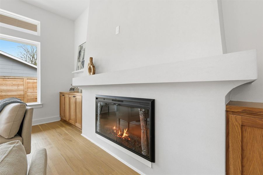A sculptural stucco fireplace serves as a refined focal point, flanked by warm white oak cabinetry that adds functional closed storage.