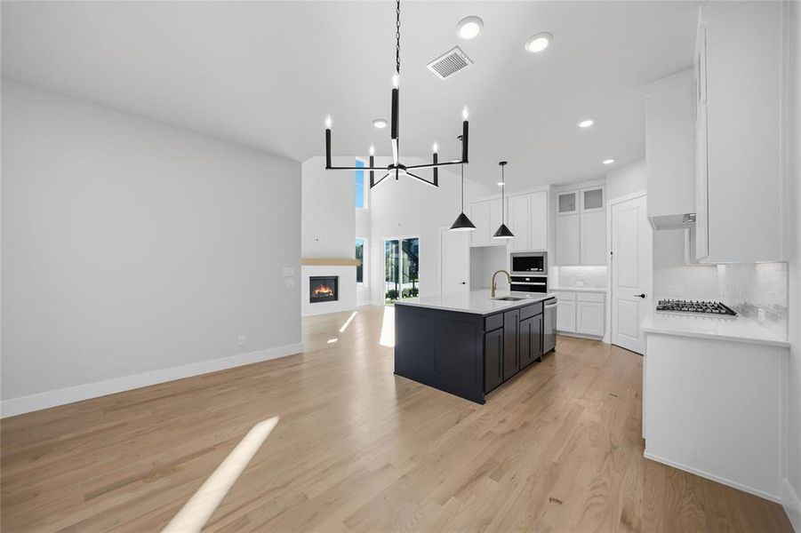 Kitchen featuring white cabinetry, a glass covered fireplace, open floor plan, hanging light fixtures, and light wood finished floors