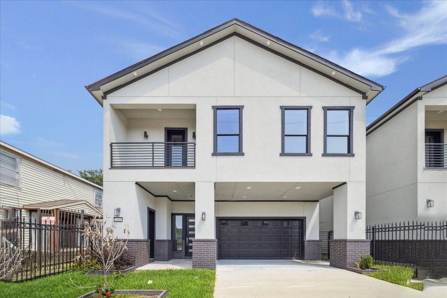 Crisp lines and contemporary detailing shape the front elevation, highlighted by light stucco paired with dark trim. The covered entry leads into a gated drive and two-car garage, combining practicality with a refined streetscape presence.