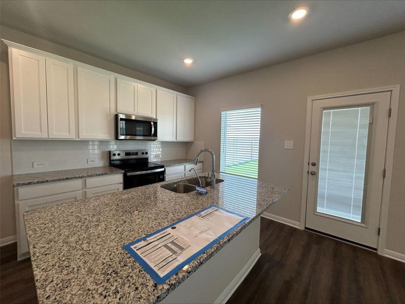 Kitchen with decorative backsplash, appliances with stainless steel finishes, white cabinetry, dark wood-style floors, and light stone counters Kitchen with decorative backsplash, appliances with stainless steel finishes, white cabinetry, dark wood-style floors, and light stone counters