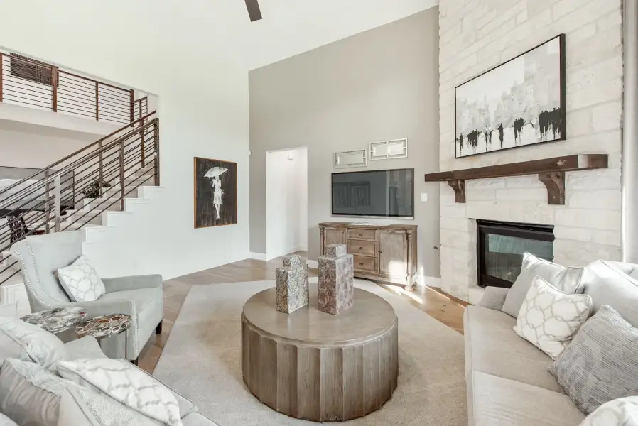 Living room with vaulted ceiling, stone fireplace, round wood coffee table, and open staircase with metal railing