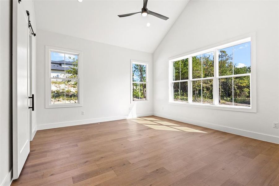 Empty room featuring high vaulted ceiling, light wood-type flooring, recessed lighting, a barn door, and ceiling fan Empty room featuring high vaulted ceiling, light wood-type flooring, recessed lighting, a barn door, and ceiling fan