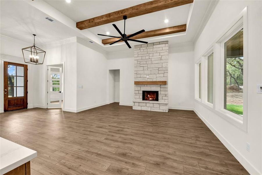 Unfurnished living room featuring wood finished floors, a fireplace, ceiling fan, beam ceiling, and a chandelier Unfurnished living room featuring wood finished floors, a fireplace, ceiling fan, beam ceiling, and a chandelier