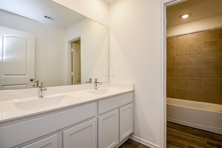 This modern bathroom features a double vanity with sleek white cabinetry and a large mirror. It includes a cozy bathtub with tiled walls, offering a clean and inviting space. This modern bathroom features a double vanity with sleek white cabinetry and a large mirror. It includes a cozy bathtub with tiled walls, offering a clean and inviting space.