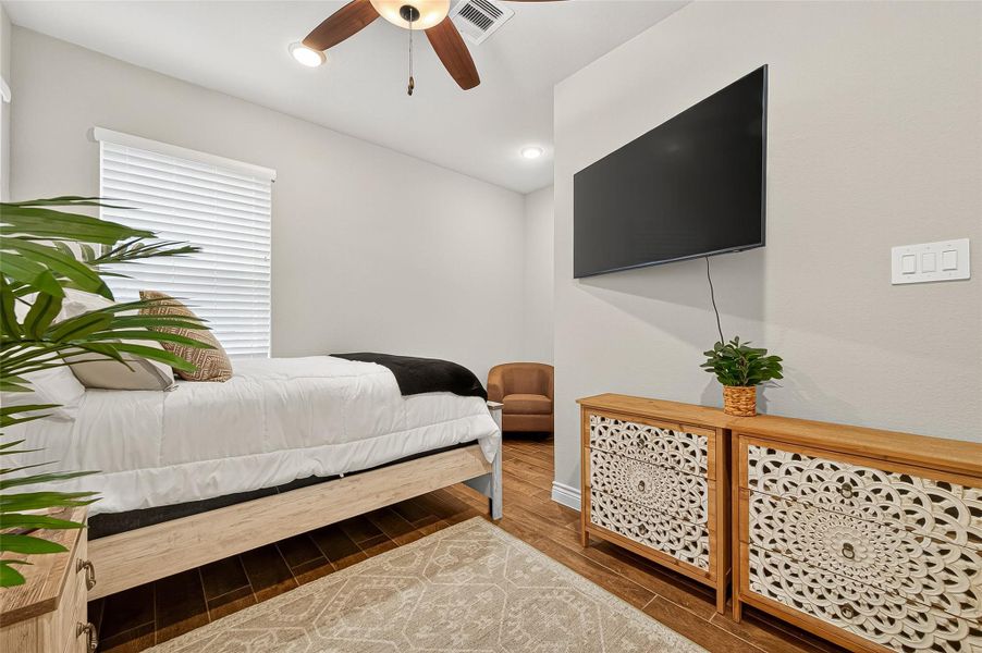 Bright and comfortable guest bedroom with neutral tones, wood-look tile flooring, and ample natural light. Bright and comfortable guest bedroom with neutral tones, wood-look tile flooring, and ample natural light.