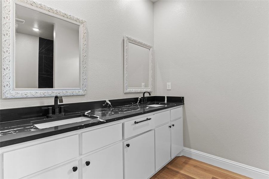 Full bath with light wood-type flooring, double vanity, and a textured wall