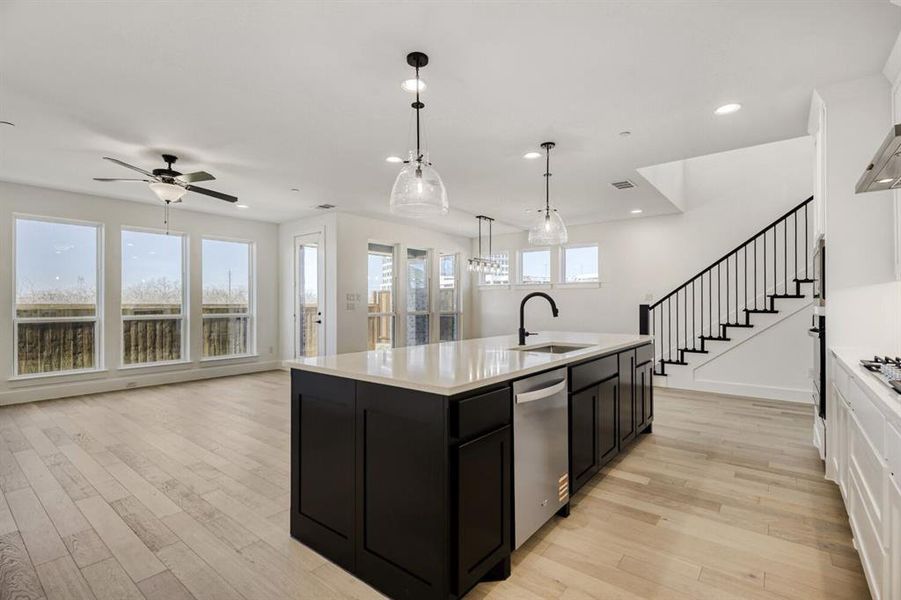 Kitchen with pendant lighting, open floor plan, light wood-type flooring, an island with sink, and dishwasher