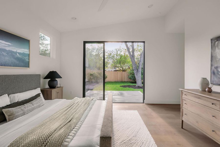 Bedroom featuring lofted ceiling, multiple windows, light wood-style floors, access to exterior, and a ceiling fan Bedroom featuring lofted ceiling, multiple windows, light wood-style floors, access to exterior, and a ceiling fan