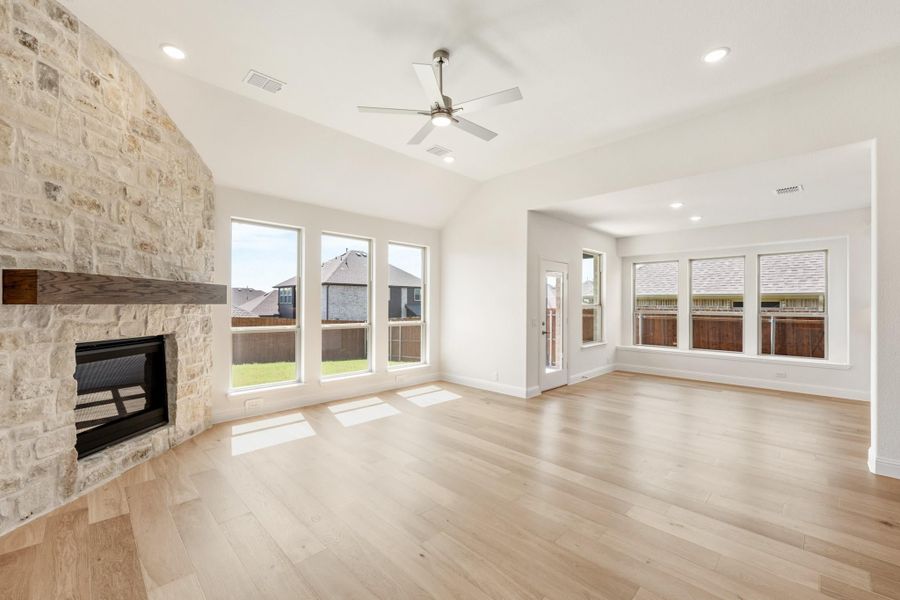 Open living room with stone fireplace, hardwood floors, vaulted ceiling, and ceiling fan Open living room with stone fireplace, hardwood floors, vaulted ceiling, and ceiling fan
