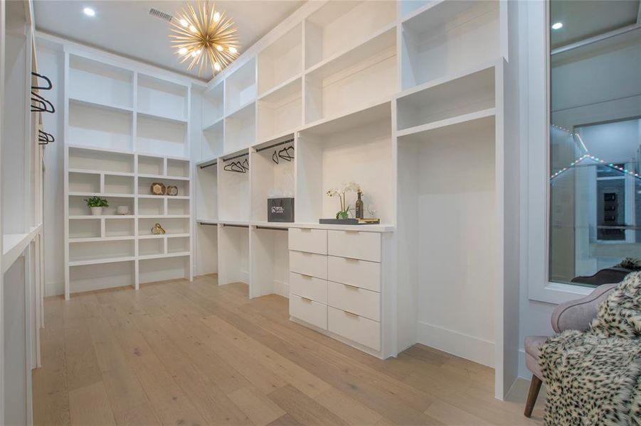 Walk in closet with light hardwood / wood-style flooring and a notable chandelier