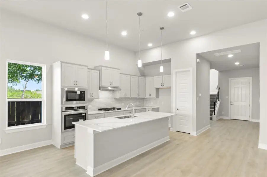 Kitchen featuring stainless steel appliances, light stone countertops, tasteful backsplash, light wood-style flooring, and a center island with sink Kitchen featuring stainless steel appliances, light stone countertops, tasteful backsplash, light wood-style flooring, and a center island with sink