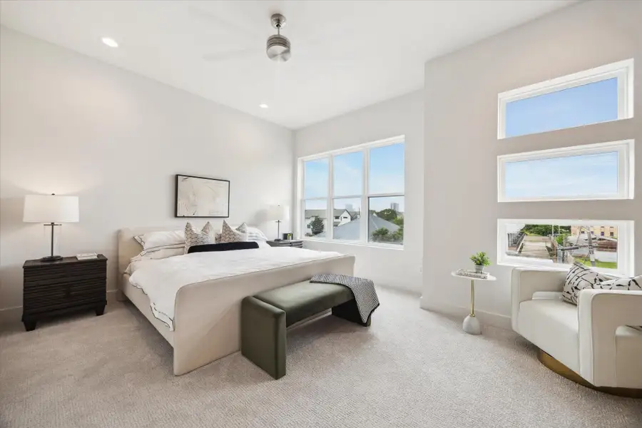 Spacious and bright bedroom with large windows offering scenic views. Features modern decor, a cozy sitting area, and neutral tones for a relaxing atmosphere.