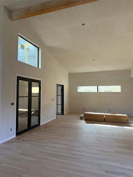 Empty room with light wood-style flooring, high vaulted ceiling, and beam ceiling Empty room with light wood-style flooring, high vaulted ceiling, and beam ceiling
