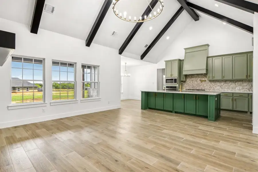 Kitchen featuring green cabinetry, a chandelier, high vaulted ceiling, decorative backsplash, and open floor plan Kitchen featuring green cabinetry, a chandelier, high vaulted ceiling, decorative backsplash, and open floor plan