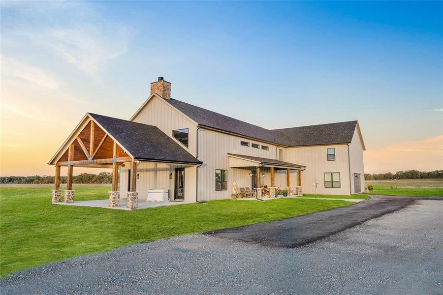 Back of house at dusk with a patio area, roof with shingles, a chimney, and a lawn