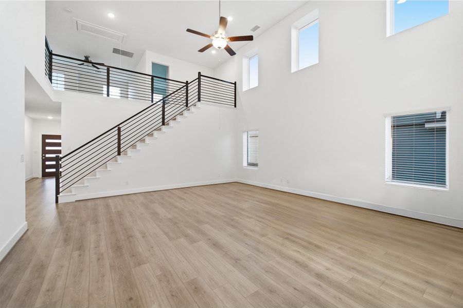 Unfurnished living room with a ceiling fan, a high ceiling, and light wood-style flooring