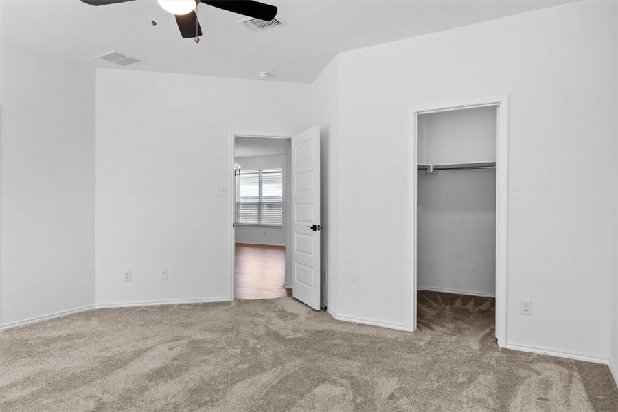 Unfurnished bedroom with a spacious closet, light carpet, and ceiling fan