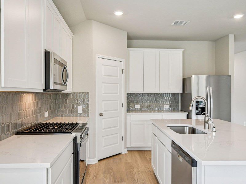 Kitchen with stainless steel appliances, light wood-style floors, a kitchen island with sink, white cabinets, and tasteful backsplash Kitchen with stainless steel appliances, light wood-style floors, a kitchen island with sink, white cabinets, and tasteful backsplash