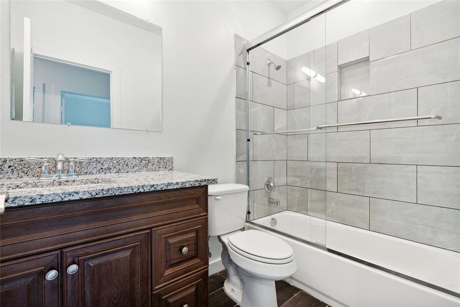 Full bathroom featuring vanity, toilet, hardwood / wood-style floors, and bath / shower combo with glass door