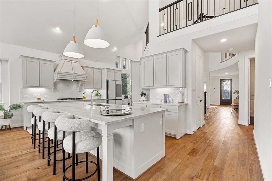 Kitchen featuring decorative backsplash, a kitchen breakfast bar, a kitchen island with sink, stainless steel gas cooktop, and premium range hood