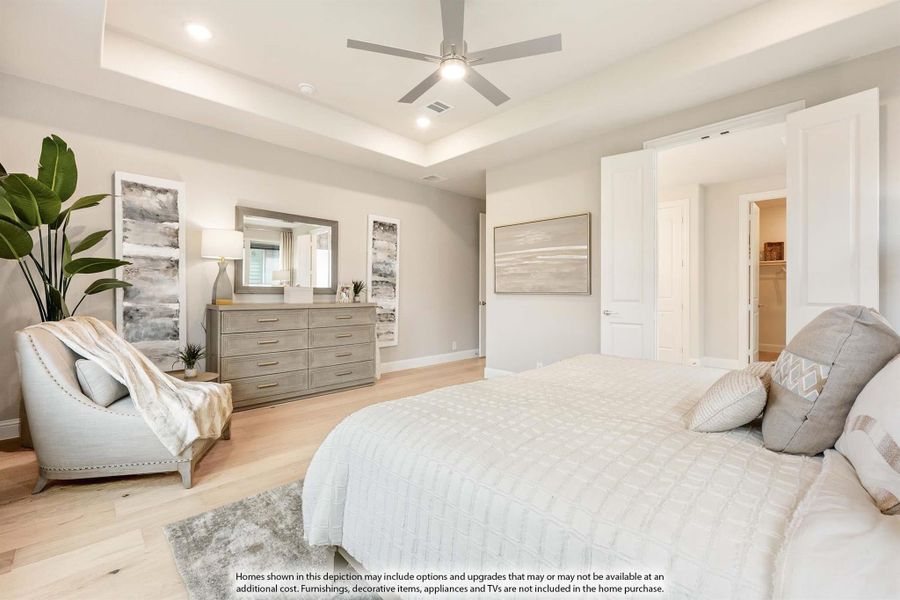 Master bedroom with tray ceiling, ceiling fan, hardwood floors, dresser with mirror, and walk-in closet entrance