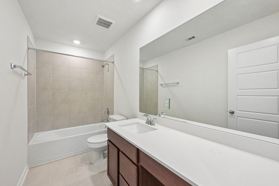 The secondary bathroom offers tile flooring, a bath/shower combination with a stylish tile surround, rich stained wood cabinetry with added knee space and elegant light countertops, a mirror, and sleek fixtures with modern finishes. The secondary bathroom offers tile flooring, a bath/shower combination with a stylish tile surround, rich stained wood cabinetry with added knee space and elegant light countertops, a mirror, and sleek fixtures with modern finishes.