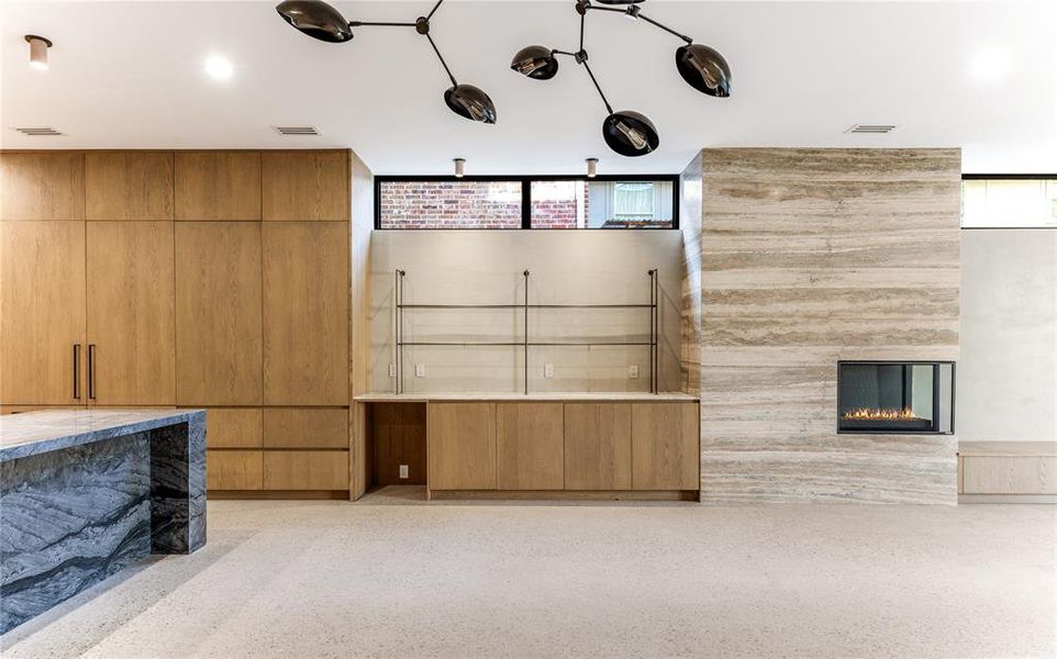 Open kitchen/living room with a bar (with hidden sink) and space for beverage or wine fridge,  fireplace and exposed aggregate floor.