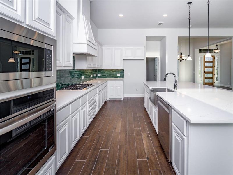 Kitchen with decorative light fixtures, stainless steel appliances, white cabinetry, wood tiled floors, and a spacious island