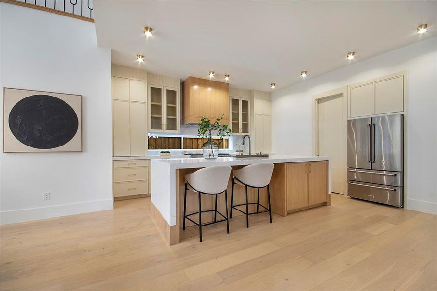Kitchen with glass insert cabinets, a kitchen breakfast bar, high quality fridge, a kitchen island with sink, and light wood finished floors Kitchen with glass insert cabinets, a kitchen breakfast bar, high quality fridge, a kitchen island with sink, and light wood finished floors