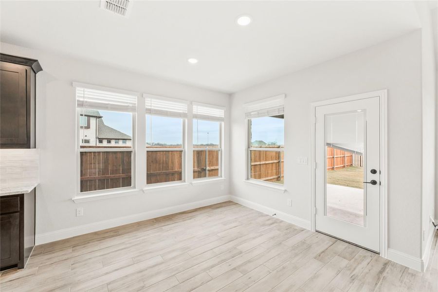 Bright dining area with light wood floors, three windows, and glass door leading to backyard Bright dining area with light wood floors, three windows, and glass door leading to backyard