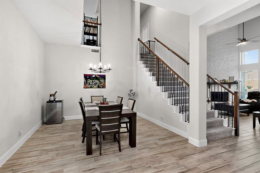 Dining area with a towering ceiling, light wood-type flooring, a chandelier, stairs, and a ceiling fan Dining area with a towering ceiling, light wood-type flooring, a chandelier, stairs, and a ceiling fan