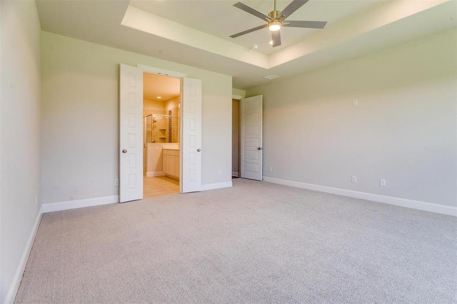 Unfurnished bedroom with a raised ceiling, ensuite bath, ceiling fan, and light colored carpet