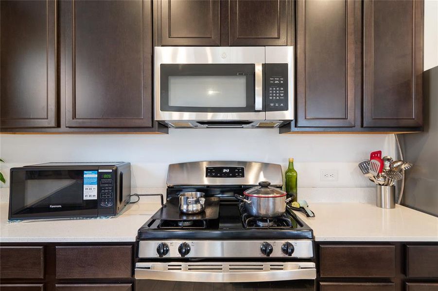 Kitchen featuring dark brown cabinets, stainless steel appliances, and light stone countertops
