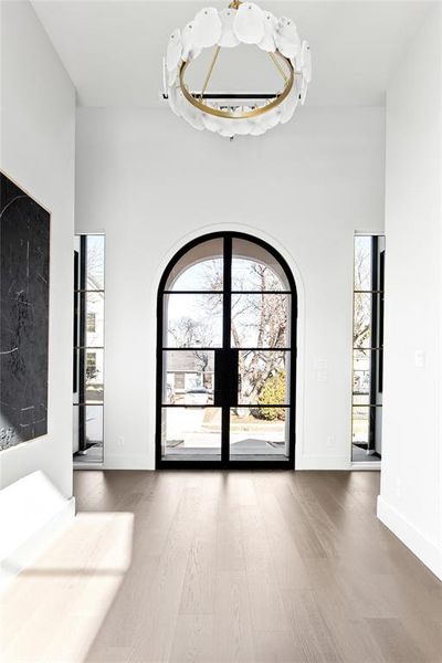 Grand entry featuring an arched double door with black framing, wood-finish flooring, and a modern chandelier