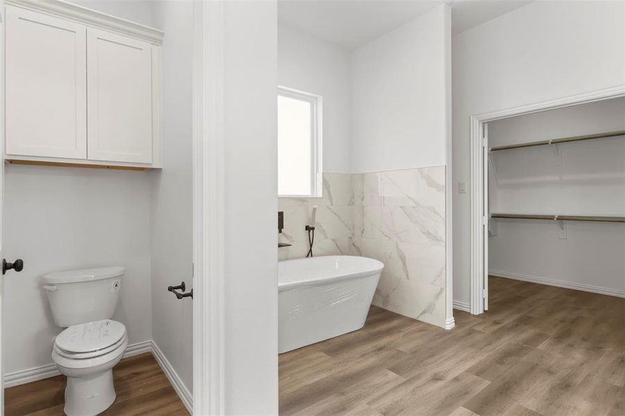 Bathroom featuring hardwood / wood-style flooring, toilet, and a tub to relax in