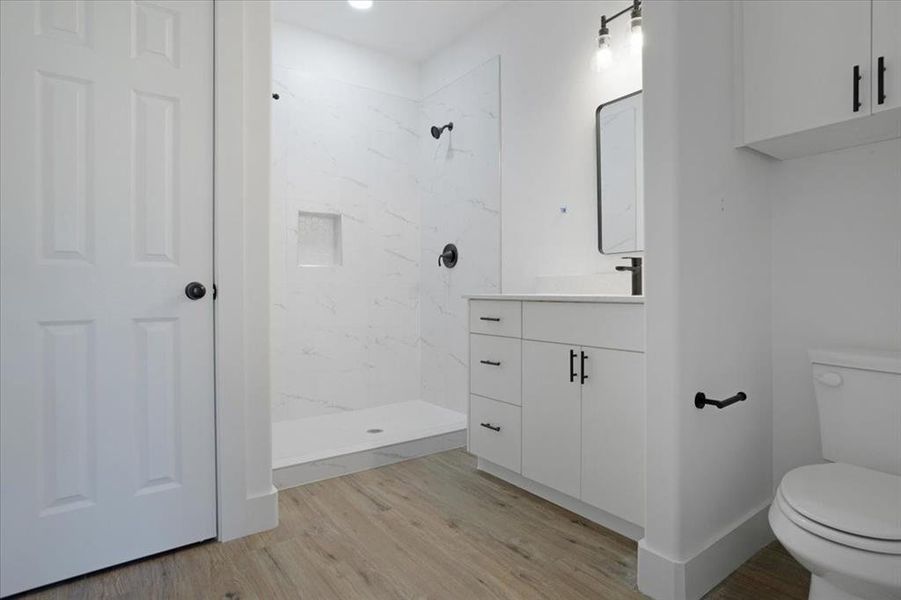 Bathroom featuring tiled shower, vanity, hardwood / wood-style flooring, and toilet