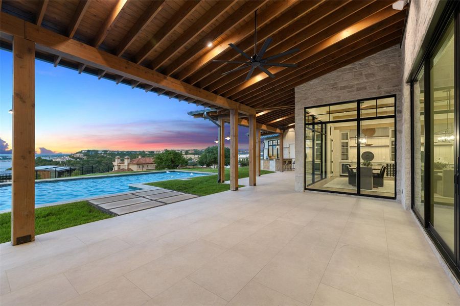 Patio terrace at dusk with a ceiling fan, a patio, and an infinity pool