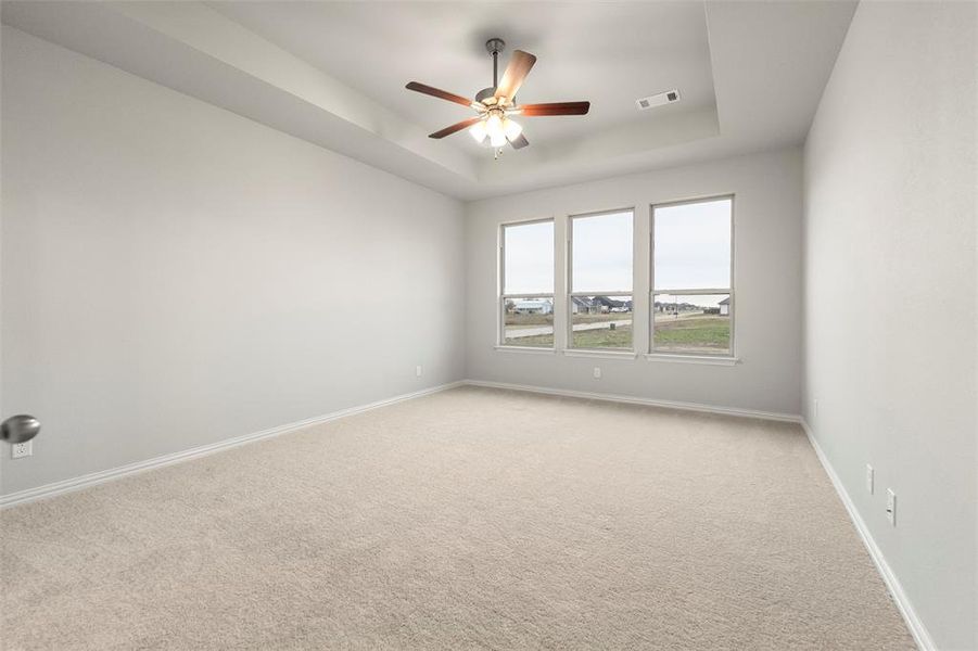 Spare room featuring a tray ceiling, light colored carpet, and a ceiling fan Spare room featuring a tray ceiling, light colored carpet, and a ceiling fan
