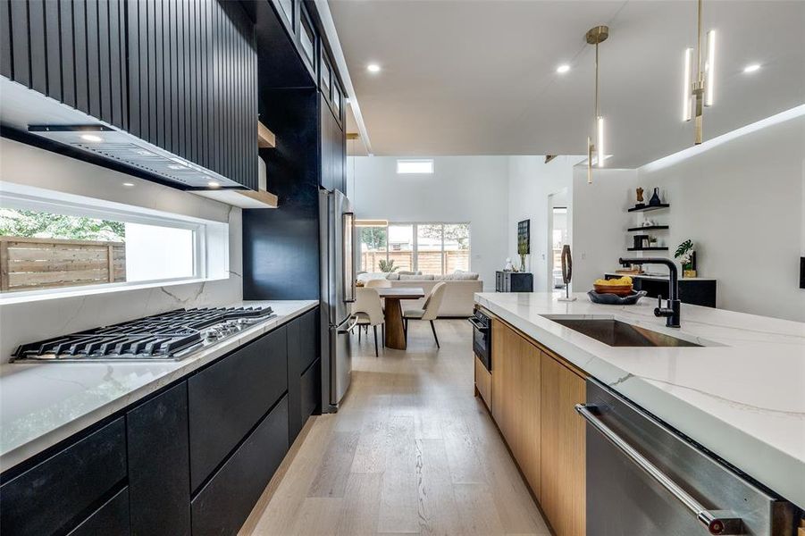 Kitchen with stainless steel appliances, light hardwood / wood-style flooring, light stone counters, decorative light fixtures, and sink