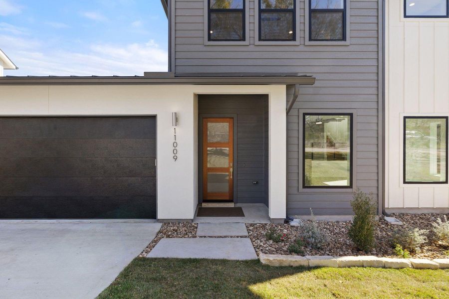 Doorway to property with board and batten siding, driveway, and a garage