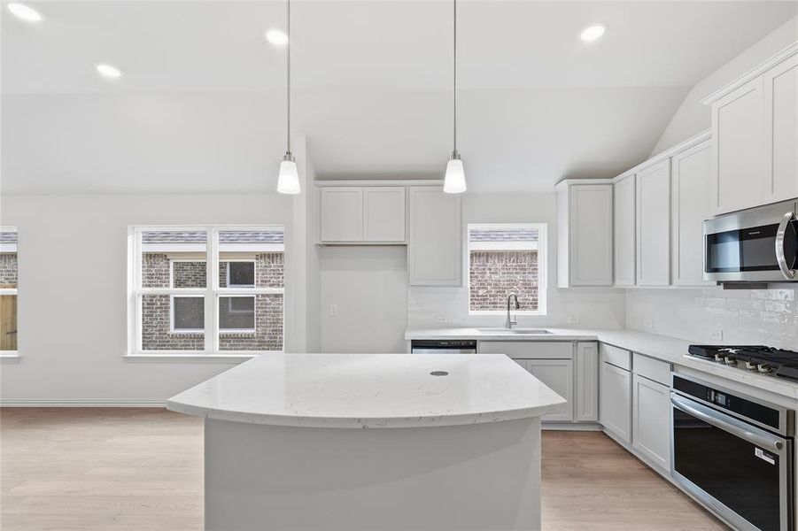 Kitchen with light stone counters, stainless steel appliances, lofted ceiling, a center island, and light wood-type flooring