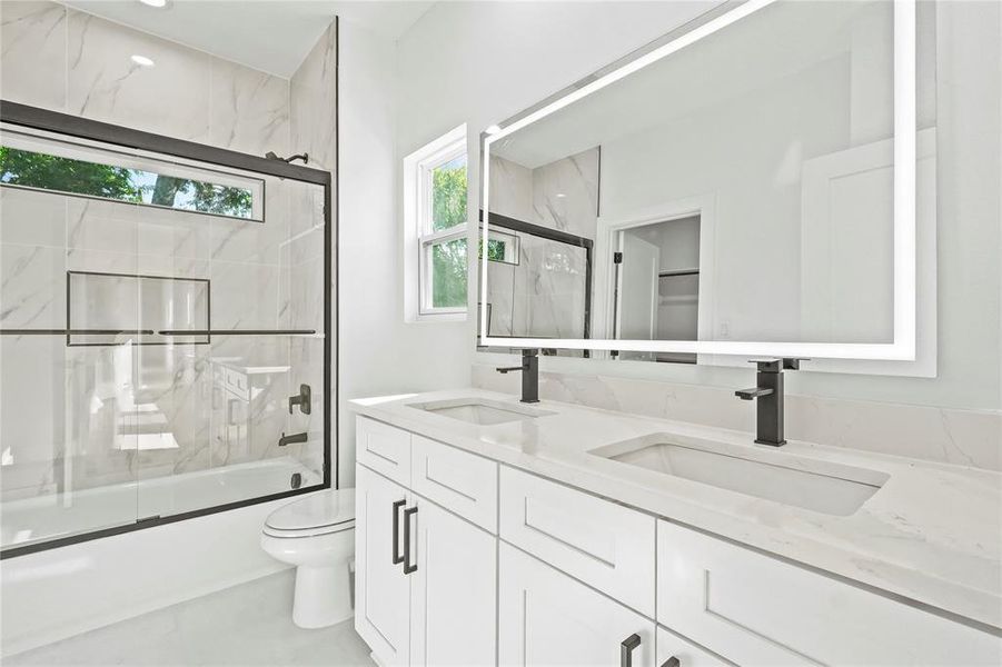 Full bath with shower / bath combination with glass door, healthy amount of natural light, and double vanity