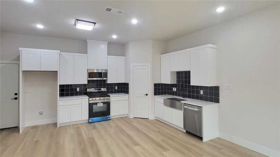 Kitchen with light wood-style floors, visible vents, white cabinetry, and stainless steel appliances