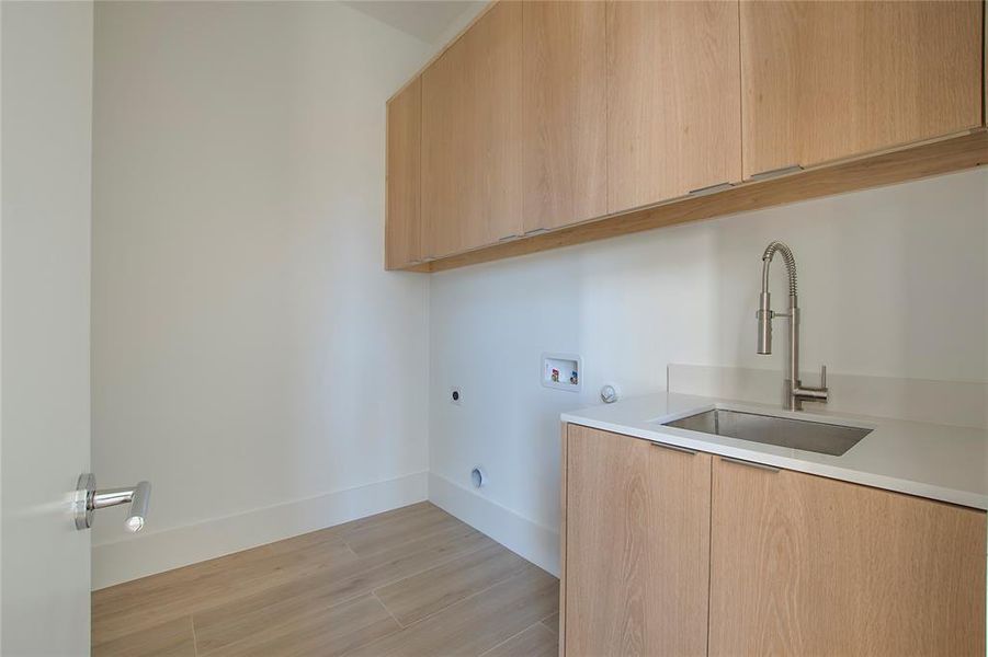 Laundry area with cabinets, electric dryer hookup, washer hookup, sink, and light hardwood / wood-style flooring