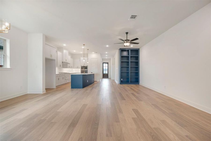 Open concept living area featuring light-toned hardwood floors, a ceiling fan, and a built-in bookshelf
