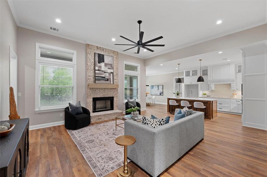Living area with a fireplace, ceiling fan, ornamental molding, and visible vents