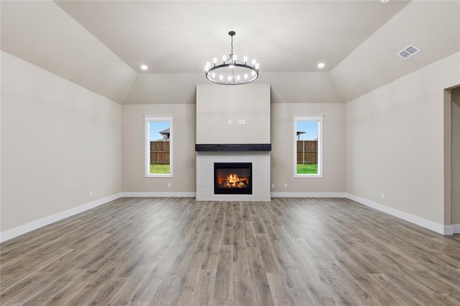 Spacious room featuring vaulted ceilings, a central fireplace with a white tile surround and dark wood mantel, recessed lighting, wood-finish flooring, and two windows Spacious room featuring vaulted ceilings, a central fireplace with a white tile surround and dark wood mantel, recessed lighting, wood-finish flooring, and two windows
