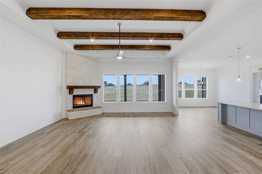 Unfurnished living room with a stone fireplace, a ceiling fan, light wood-type flooring, beamed ceiling, and ornamental molding
