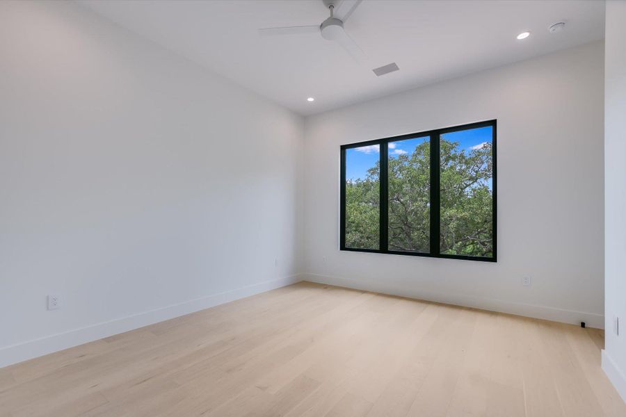 A spacious room featuring wood flooring, recessed lighting, and a window with vibrant green views.